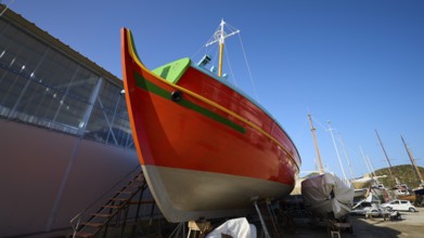 Side view of an orange-coloured boat in a shipyard under a blue sky, Diakofti boatyard, new