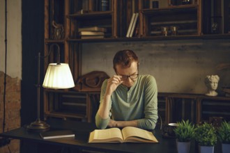 In a serene study space, a thoughtful man sits at a desk, deeply engaged in reading a book. Soft