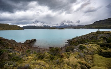 Cloudy mountain range Cuernos del Paine, shore of the blue lake Lago Pehoe in the evening light,