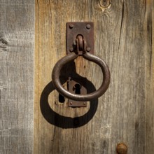 A weathered wooden door showcases an ornate metal knocker and an antique keyhole, reflecting the
