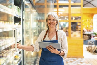 Smiling senior supermarket employee taking notes on a digital tablet while checking products in a