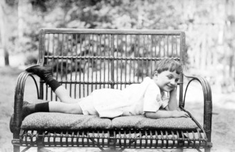 Young boy lying on a bench outdoors, 1920s, A boy lies smiling on a comfortable couch in the
