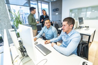 Two customer service representatives working on computer in a busy call center, assisted by their