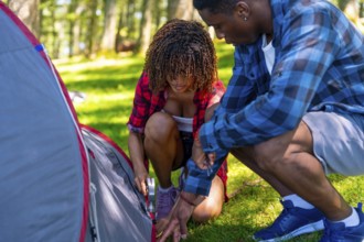 Young couple setting up a camping tent on a grassy campsite in a serene forest, embracing the joys
