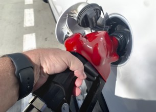 Male hand holding gas pump nozzle pumping gas into vehicle