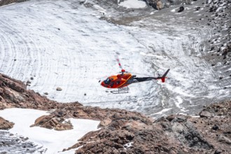 Red helicopter flies over glaciers in the mountains, Stubai Alps, South Tyrol, Italy
