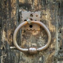 A round metal door knocker hangs on an aged wooden door, showcasing its rustic texture and worn