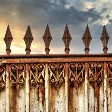 A rusty ornate gate stands tall, featuring intricate designs and pointed spikes. The backdrop shows