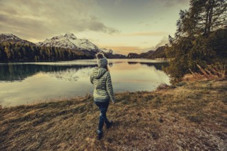 Woman by the lake in autumn Engadine in Switzerland with snow-covered mountain peaks