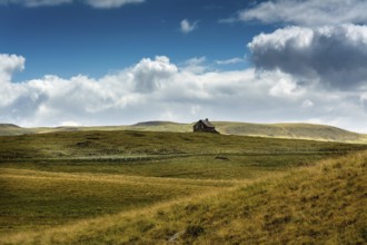 Ruined stone cottage stands alone on a grassy hillside under a partly cloudy sky in a remote