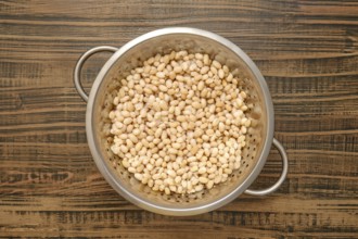 Dried white beans being rinsed in a metal colander on a wooden kitchen countertop