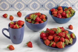 Several blue bowls and a cup full of fresh strawberries scattered on a marble top
