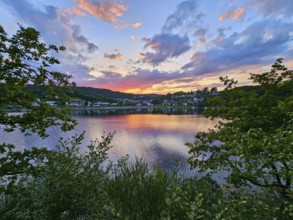 Colourful sunset over a calm lake, surrounded by trees and reflecting clouds in the sky, summer,