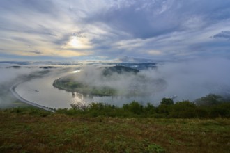 River landscape with wafts of mist and rolling hills in the background. Calm atmosphere, summer,