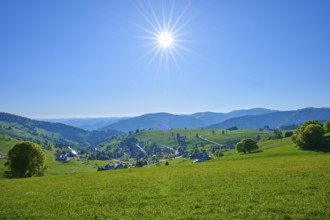 Sunny panoramic view of a village surrounded by green hills under a clear sky, spring,