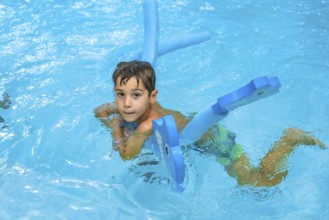 Young boy enjoying summer days, playing with a blue floating toy in a refreshing blue pool under