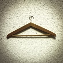 A wooden clothes hanger is resting on a textured wall, showcasing its natural finish and design.