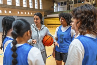 Female basketball coach holding ball and explaining game strategy to her team during training in a