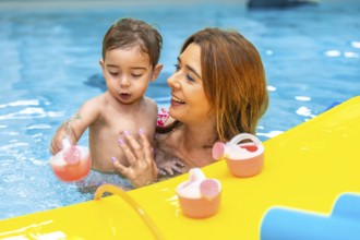 Mother and baby daughter enjoying playful moments with colorful toys in a swimming pool, creating