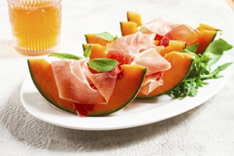 Cantaloupe melon with prosciutto and fresh basil, on a white plate, natural light