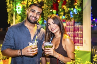 Young couple smiling and holding cocktails at a night market, enjoying the vibrant atmosphere and