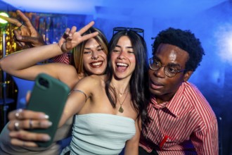 Happy multi ethnic friends taking a selfie while partying in a nightclub, making peace signs and