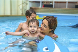 Mother and two sons enjoying time together, playing with inflatable toy in home swimming pool,