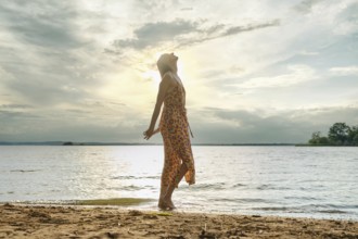 Woman enjoying serenity by the lakeside at sunset with vibrant dress flowing in the breeze
