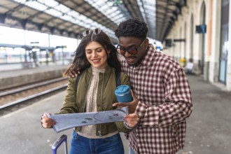 Young multi ethnic couple consulting a map on a train station platform, planning their next