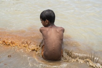 A boy sits in the bank of Brahmaputra River as he bathe to seek relief from the intense summer heat