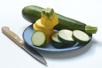 Green and yellow courgettes on a plate with a knife, Cucurbita pepo