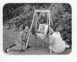 Women with baby on swing, 1930s, Two woman kneeling smiling in front of a baby in a swing, sitting