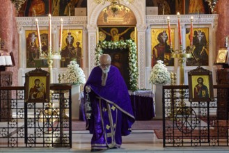 Priest in purple robe walking past an altar with icons and burning candles, Church of the