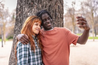 Interracial couple taking a selfie with a smartphone in a park, smiling and enjoying a moment
