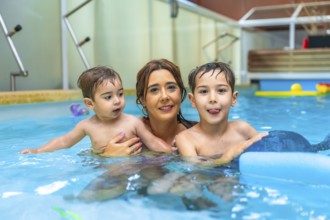 Happy mother embracing her two children while playing and smiling in a swimming pool during summer