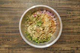 Overhead view of a bowl with chopped herbs, diced onions, and various spices added to minced meat