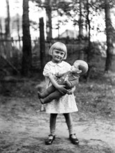 Girl with doll, 1930, Cheerful girl holding a doll in a wooded area on a sunny day, Historical