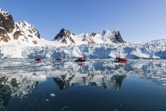Group of Zodiacs in front of glacier and mountain range with snow, sea, Fugelfjorden, Spitsbergen,