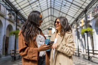 Two cheerful businesswomen are enjoying a moment together, using a smartphone and holding a