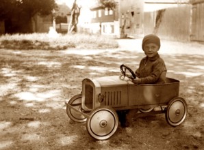 My first car, 1930s, child in a toy car on a sunny street, happy and carefree, historical photo