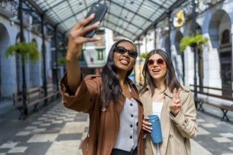 Two female friends taking a selfie in a covered walkway in a city center, one is holding a reusable