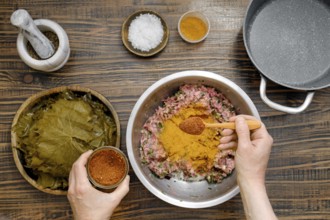 Home cook prepares dolma by adding pepper mix into minced meat. Pickled grape leaves are ready for