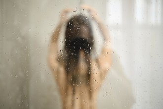 A woman stands in the shower with her hair down, enjoying a peaceful moment. Water cascades down