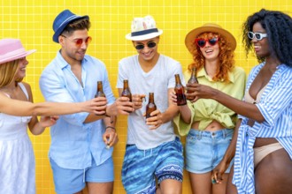 Group of cheerful young friends toasting with beer bottles while standing together against a