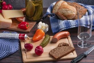 Rustic arrangement with sausage, cheese, vegetables, mustard and bread on a laid table