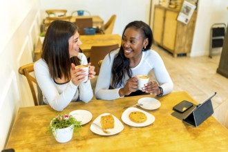 Two female friends enjoying coffee and snacks while chatting and laughing together at a cozy cafe