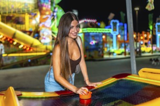 Happy woman playing air hockey at amusement park, enjoying nightlife entertainment with colorful