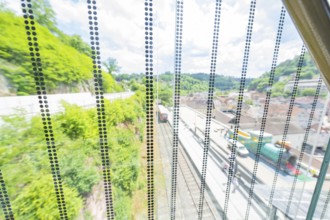 View through a permeable wall of railway tracks and green hills in the background, Zob extension