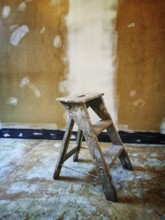 A worn wooden ladder rests on an uneven floor in a room with a freshly painted wall. The
