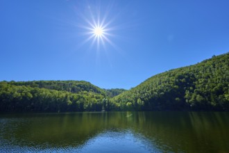 Bright sun over a calm lake with green hills and blue sky, summer, Rursee, Obersee, Simmerath,